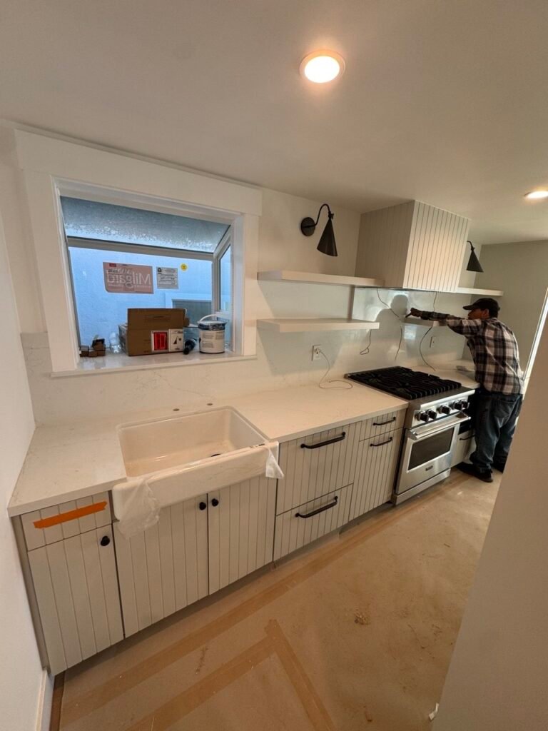This custom kitchen cabinetry project in Fallbrook, California was designed to bring warmth, character, and timeless craftsmanship into the heart of the home. The kitchen features elegant green shaker cabinets paired with premium custom details and functional storage solutions throughout. Our team designed and built fully custom cabinetry, including a beautifully integrated coffee station, a dedicated laundry area, and custom storage tailored to the homeowner’s lifestyle. Every cabinet was built to maximize organization while maintaining a clean, sophisticated design. One of the standout features of this project is the custom alder wood range hood, finished to complement the surrounding cabinetry and add natural warmth to the space. On both sides of the kitchen window, we installed solid alder floating shelves, creating an inviting focal point while providing stylish open storage. Built with premium materials, soft-close hardware, and precision craftsmanship, this project showcases the perfect balance between traditional shaker styling and modern functionality. Every detail was carefully planned and executed to create a kitchen that is both beautiful and built to last. This Fallbrook custom kitchen reflects our commitment to exceptional craftsmanship, personalized design, and high-quality custom cabinetry for homeowners throughout San Diego County.